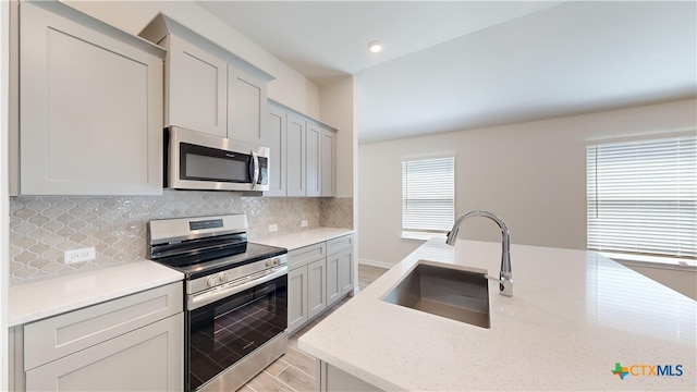 kitchen featuring a wealth of natural light, light stone countertops, sink, and appliances with stainless steel finishes