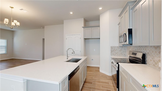 kitchen featuring a chandelier, sink, stainless steel appliances, and an island with sink