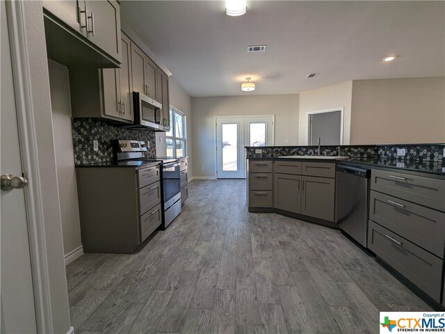 kitchen featuring stainless steel appliances, hardwood / wood-style flooring, gray cabinetry, and backsplash