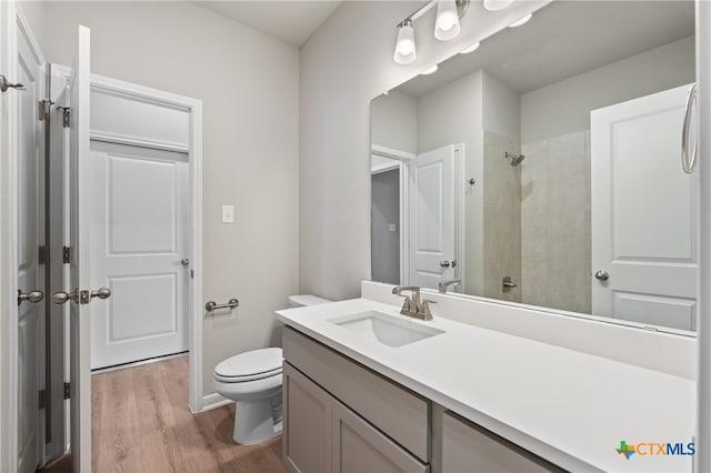 bathroom featuring a tile shower, wood-type flooring, toilet, and vanity