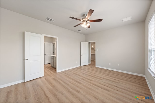 unfurnished bedroom with light wood-type flooring, multiple windows, ceiling fan, and connected bathroom