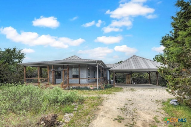 farmhouse-style home featuring covered porch, dirt driveway, a carport, and metal roof