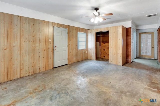 unfurnished bedroom featuring concrete floors, visible vents, wood walls, and ceiling fan