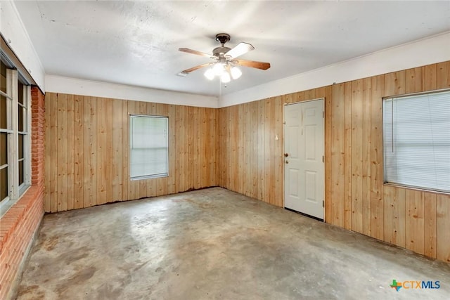 empty room featuring a ceiling fan, wood walls, and unfinished concrete floors