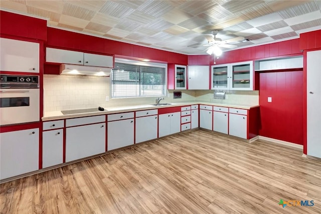 kitchen with black electric cooktop, oven, light wood-style flooring, ceiling fan, and light countertops