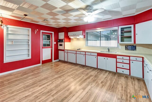 kitchen with oven, light wood-style flooring, a sink, built in shelves, and backsplash