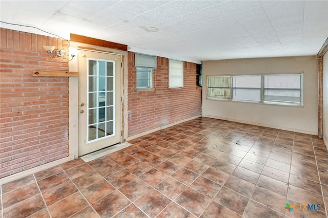 tiled empty room featuring brick wall and baseboards
