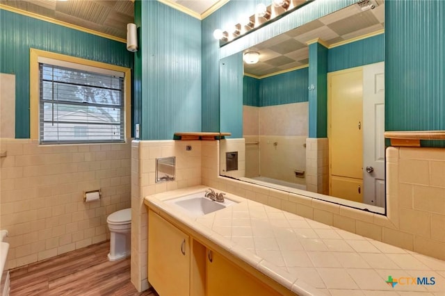 bathroom with toilet, tile walls, wood finished floors, vanity, and ornamental molding