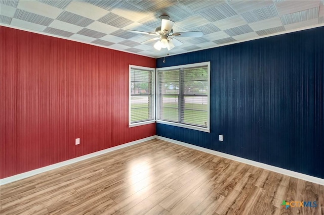 spare room featuring wood finished floors, wood walls, baseboards, and ceiling fan