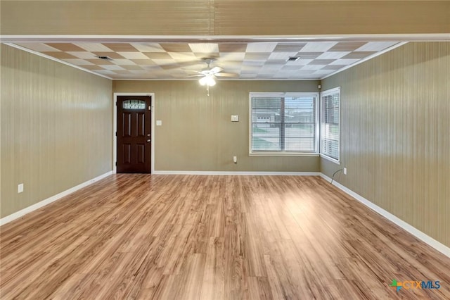 interior space featuring baseboards, a ceiling fan, wooden walls, and light wood-type flooring