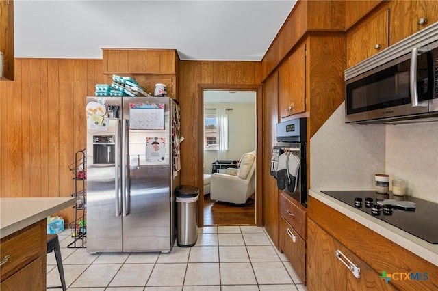 kitchen with light tile patterned floors, light countertops, brown cabinetry, wooden walls, and black appliances