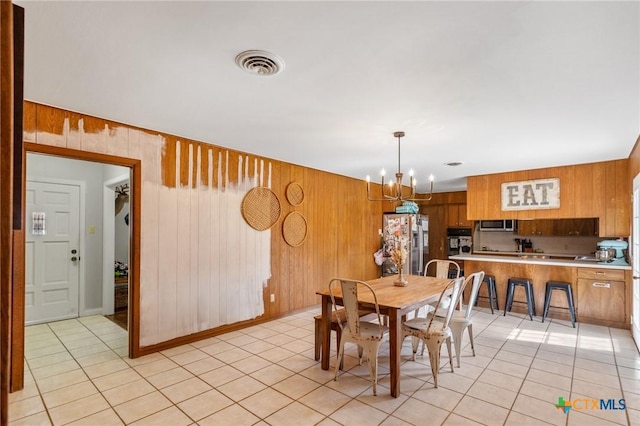 dining room with wooden walls, light tile patterned flooring, visible vents, and a notable chandelier