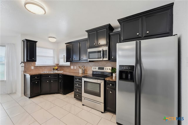 kitchen featuring sink, tasteful backsplash, stone countertops, light tile patterned floors, and appliances with stainless steel finishes