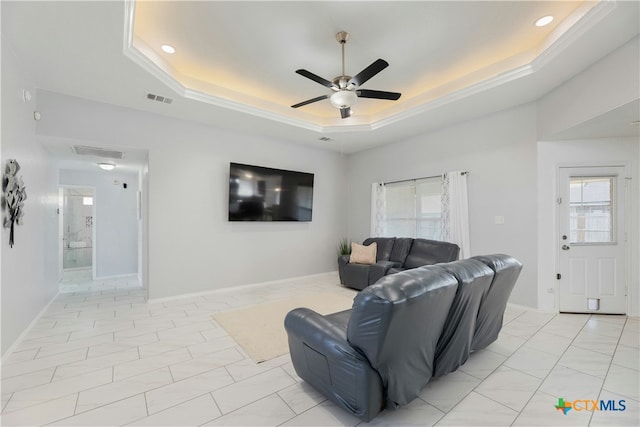 living room with a raised ceiling, plenty of natural light, and ceiling fan