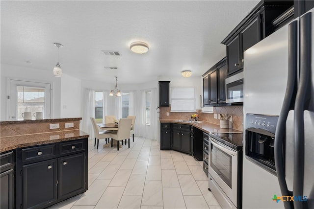 kitchen with appliances with stainless steel finishes, decorative light fixtures, sink, decorative backsplash, and dark stone counters