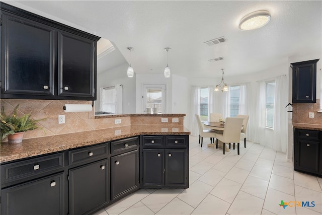 kitchen featuring decorative backsplash, a notable chandelier, hanging light fixtures, and stone counters