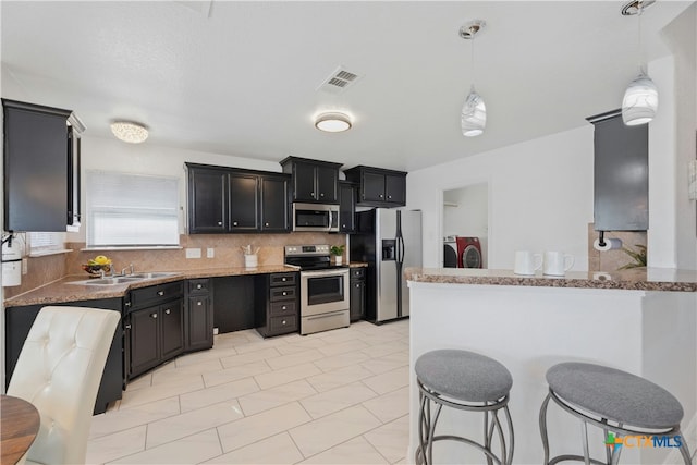 kitchen featuring light stone counters, washing machine and clothes dryer, stainless steel appliances, and decorative light fixtures