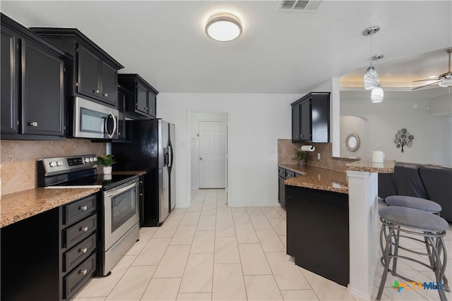 kitchen featuring a breakfast bar area, ceiling fan, hanging light fixtures, stainless steel appliances, and decorative backsplash