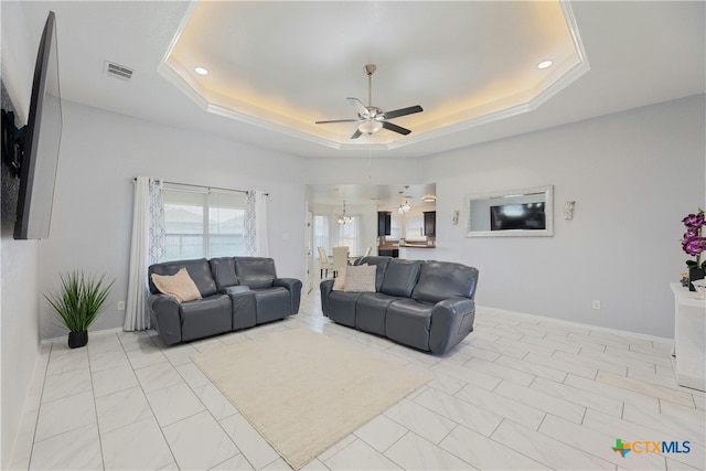 living room featuring ceiling fan with notable chandelier, a raised ceiling, and light tile patterned flooring