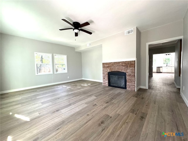 unfurnished living room with ceiling fan, a stone fireplace, and wood-type flooring