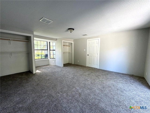 unfurnished bedroom with carpet flooring, multiple closets, and a textured ceiling