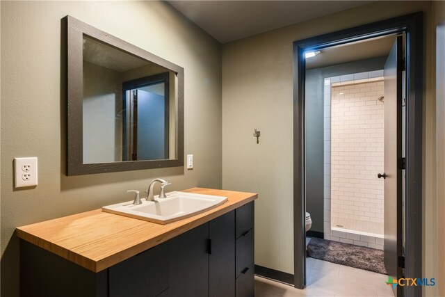 bathroom with toilet, tiled shower, tile patterned floors, and vanity