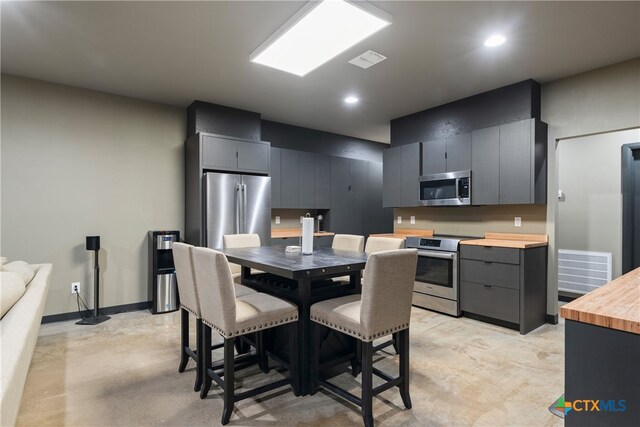 kitchen with stainless steel appliances, wooden counters, a breakfast bar area, and gray cabinetry