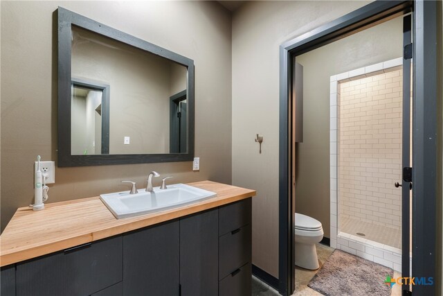 bathroom with a tile shower, vanity, and toilet