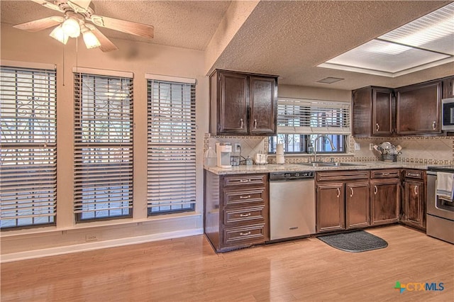 kitchen featuring stainless steel appliances, tasteful backsplash, light wood-style flooring, a sink, and dark brown cabinets