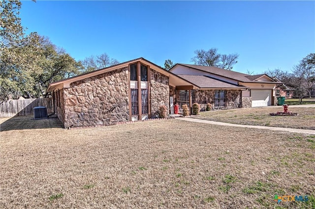 view of front of house featuring central air condition unit, fence, a garage, stone siding, and a front lawn