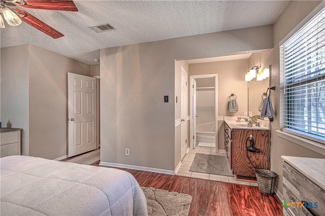 bedroom with a textured ceiling, wood finished floors, visible vents, and connected bathroom