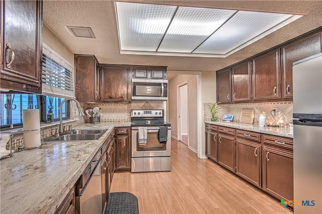 kitchen with dark brown cabinetry, stainless steel appliances, a sink, light wood-type flooring, and decorative backsplash