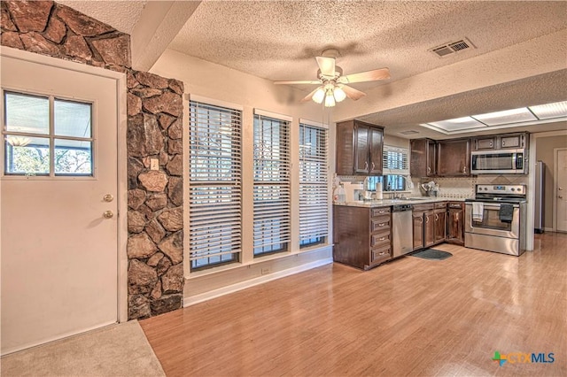 kitchen featuring stainless steel appliances, light countertops, visible vents, dark brown cabinets, and light wood-type flooring