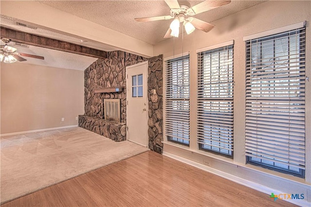 unfurnished living room featuring a textured ceiling, ceiling fan, a stone fireplace, vaulted ceiling with beams, and wood finished floors