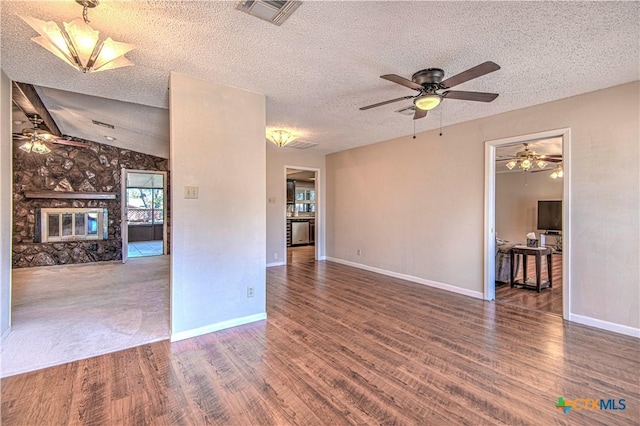 spare room featuring a large fireplace, visible vents, lofted ceiling, wood finished floors, and a textured ceiling