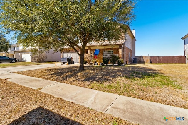 view of property hidden behind natural elements with driveway, brick siding, central AC unit, fence, and a front yard