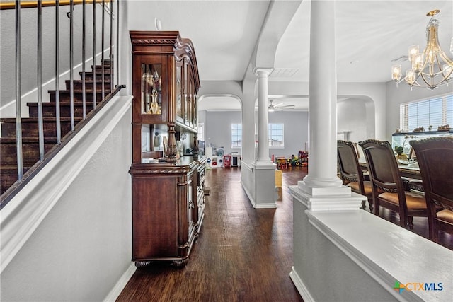 interior space featuring baseboards, arched walkways, stairway, dark wood-style flooring, and ornate columns