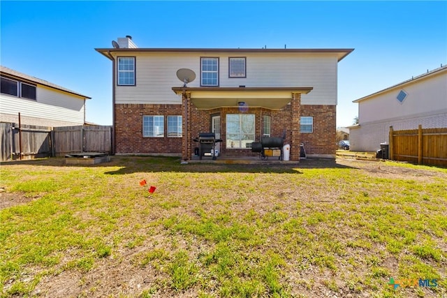 rear view of property featuring brick siding, a lawn, and fence