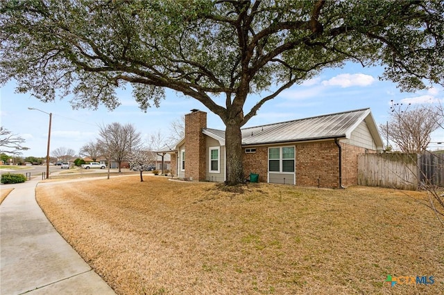 view of front of home featuring metal roof, brick siding, fence, a chimney, and a front yard