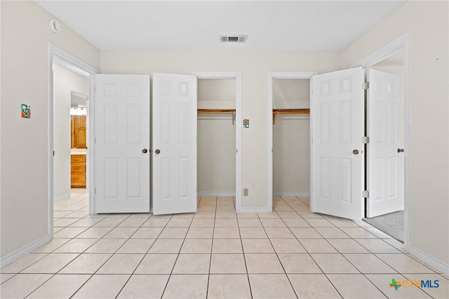 unfurnished bedroom featuring baseboards, visible vents, two closets, and light tile patterned flooring