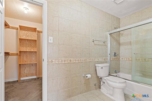 bathroom featuring toilet, shower / bath combination with glass door, tile patterned flooring, a textured ceiling, and tile walls