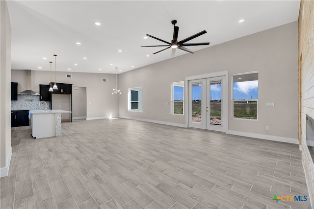 unfurnished living room with ceiling fan with notable chandelier, sink, and light wood-type flooring