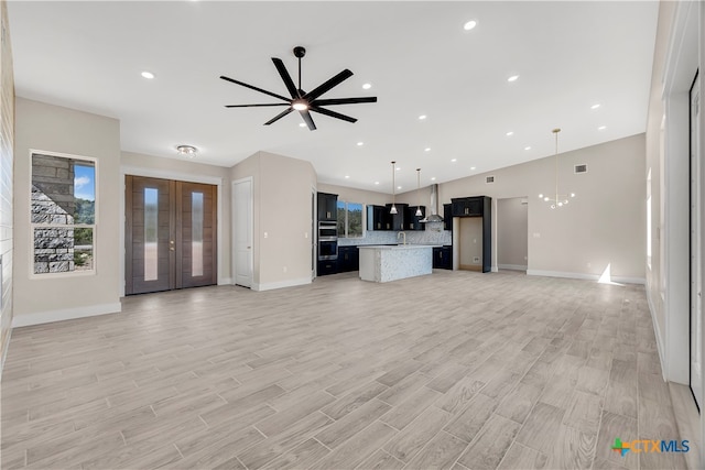 unfurnished living room featuring light wood-type flooring, ceiling fan with notable chandelier, and sink