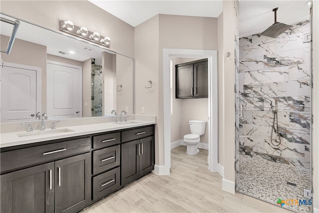 bathroom with wood-type flooring, vanity, toilet, and a tile shower