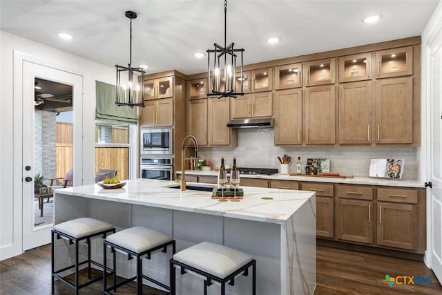 kitchen with light stone countertops, dark hardwood / wood-style flooring, stainless steel appliances, a center island with sink, and an inviting chandelier