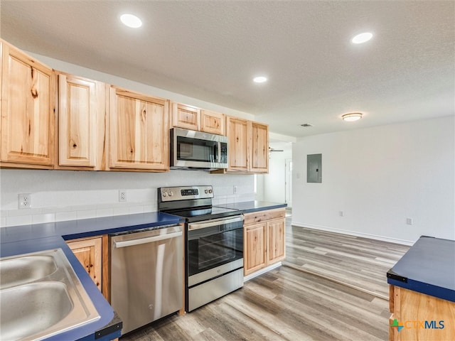 kitchen with electric panel, wood-type flooring, a textured ceiling, light brown cabinetry, and appliances with stainless steel finishes