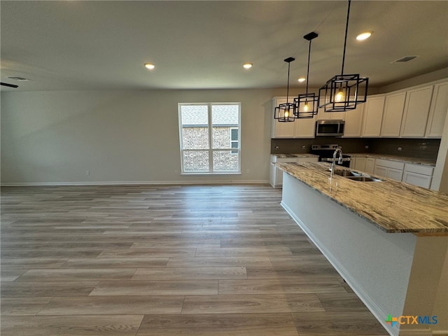 kitchen featuring light stone counters, stainless steel appliances, decorative light fixtures, sink, and white cabinets