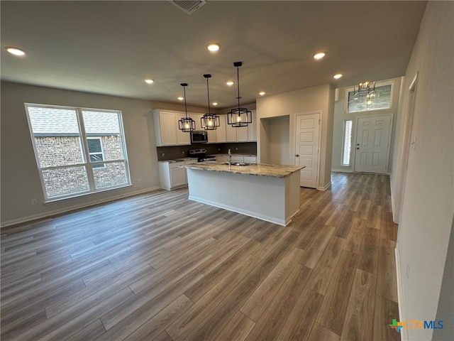 kitchen with stainless steel appliances, hardwood / wood-style flooring, sink, a kitchen island with sink, and white cabinetry