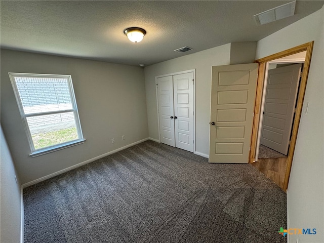 unfurnished bedroom with a closet, a textured ceiling, and dark carpet