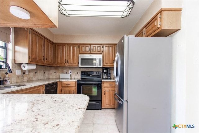 kitchen with light tile patterned floors, decorative backsplash, brown cabinetry, a sink, and black appliances